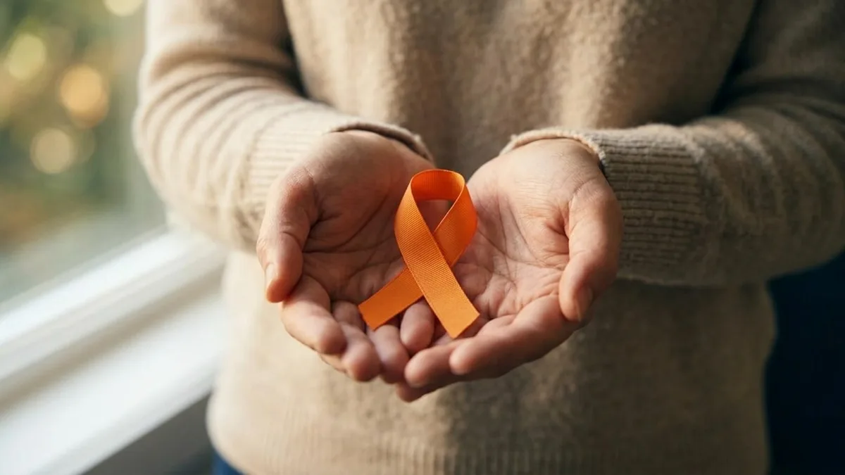 An orange awareness ribbon held in cupped hands in soft daylight